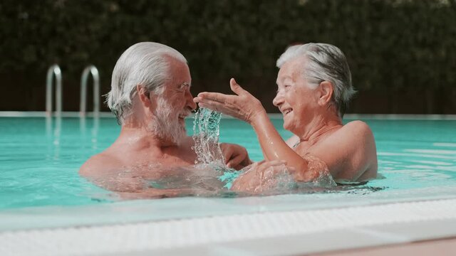 Couple of two happy seniors having fun and enjoying together in the swimming pool smiling and playing. Happy people enjoying summer outdoor in the water
