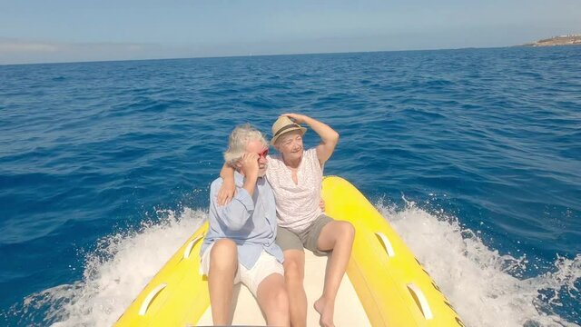 Beautiful and cute couple of seniors or old people in the middle of the sea driving and discovering new places with small boat. Mature woman holding a phone and taking a selfie with hew husband
