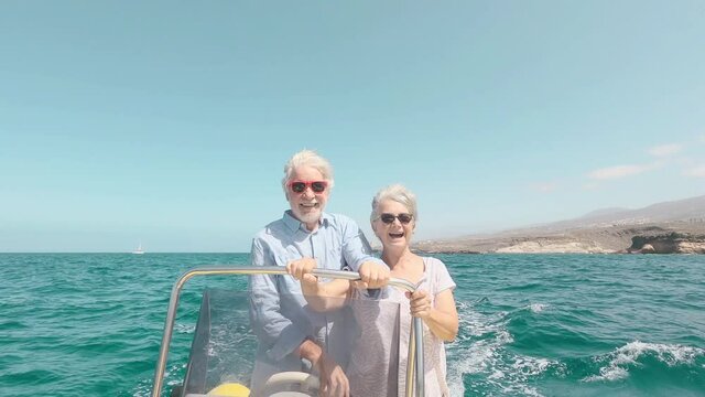 Beautiful and cute couple of seniors or old people in the middle of the sea driving and discovering new places with small boat. Mature woman holding a phone and taking a selfie with hew husband
