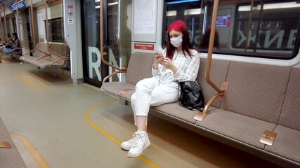 Moscow, Russia August 25, 2021 Beautiful red-haired student girl in subway in covid19 face mask and chatting on smartphone in social networks.Viral infection pandemic influenza coronavirus 2019-ncov