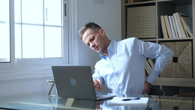 Close up rear view stressed young man touching lower back feeling discomfort, suffering from sudden pain due to sedentary lifestyle or long computer overwork in incorrect posture at home office.
