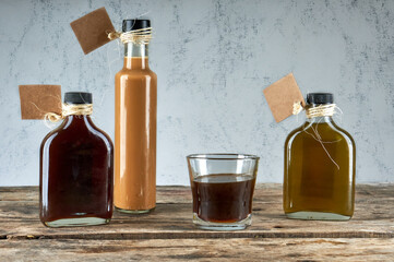 Bottles and glass with handmade liquor on wooden table with empty labels . Artisan alcoholic drinks. horizontal