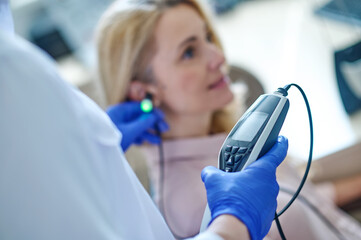 Experienced audiologist measuring the patients auditory acuity with an audiometer - obrazy, fototapety, plakaty