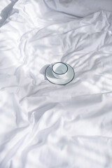 Cup and saucer on crumpled white bed linen