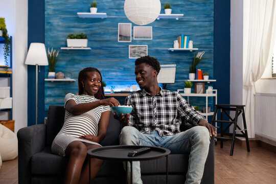 POV Of Black People Expecting Baby Relaxing At Home. African American Couple With Pregnancy Watching Television, Looking At Camera In Living Room. Young Afro Woman Being Pregnant