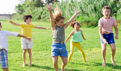 Fototapeta premium Group of children, boys and girls, jumping together on green grass in a park on sunny day