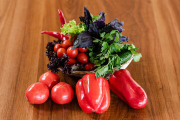 Red tomatoes, cucumbers, red paprika peppers on a wooden table surface