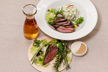 Fried beef on a plate with ingredients for okroshka, herbs and a decanter of kvass. Restaurant cooking concept