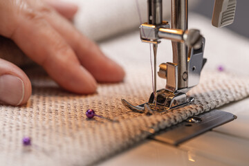 Sewing machine foot on fabric with needle and thread ready forwork. Operator's hand on the material, close-up.