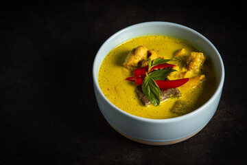 Thai food yellow curry with chicken in blue bowl on dark tone background.
