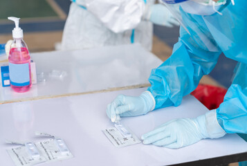 Medical personnel wear PPE holding Rapid kits of Covid-19 on white table.