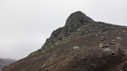 The top of the mountain, devoid of vegetation, against the background of a foggy sky. Volcanic rocks are scattered on the slopes. Kamchatka. Mount Camel