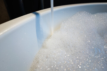 Water flowing from vintage designed tap into a bathtub with fully bubble foam, cleaning and relaxaing spa concept. Interior object photo. Close-up and selective focus in lowlight condition.