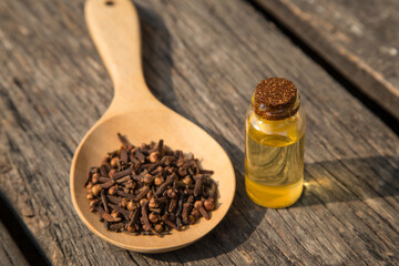 clove in wooden spoon and a bottle of essential oil on old wooden plate.
