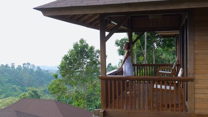Side view of a balcony of a country house with a woman wrapped with white towel around her entering...