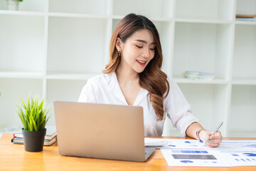 Young asian business woman working on computer laptop in office room with paperwork document on desk