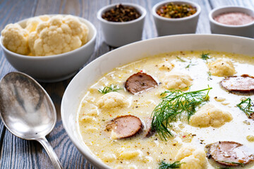 Cauliflower soup with sausages on wooden table
