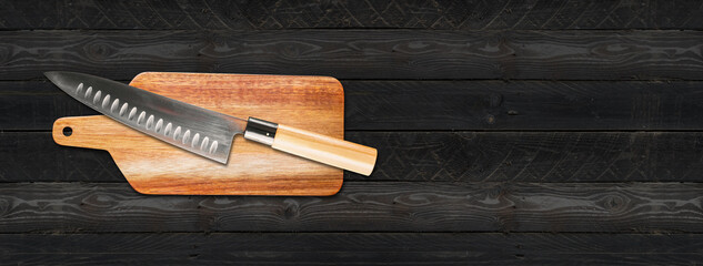 Traditional Japanese gyuto chief knife on a cutting board. Black wooden background banner