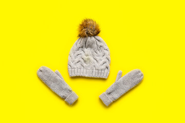 Stylish warm hat and mittens on color background
