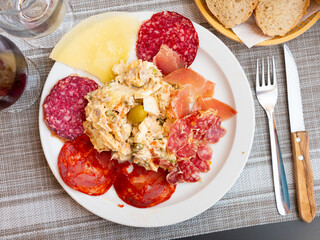 Plate with coldcuts from sliced salami, fuet, chorizo, jamon iberico and hard cheese served with russain salad. Popular Spanish entremets
