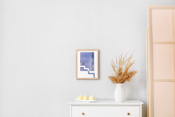 Chest of drawers with vase and candles near light wall