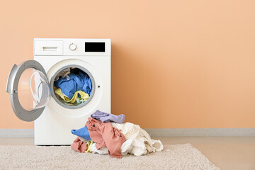 Modern washing machine with laundry near color wall