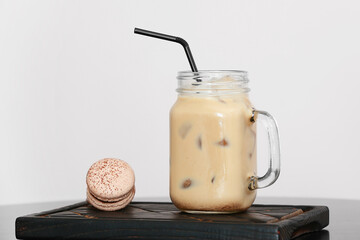 Wooden board with mason jar of tasty iced coffee and macaroons on table