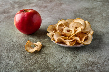 Dehydrated apples chips on plate and apple fruit on wooden background. Close up
