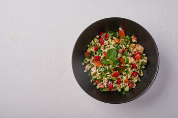 Middle Eastern traditional salad tabbouleh made of bulgur or couscous, poultry meat, parsley, mint, lemon, tomatoes and pepper, top view, copy space