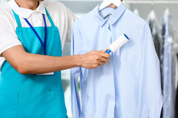 Male worker cleaning clothes with lint roller at modern dry-cleaner's