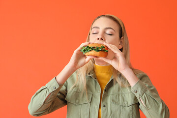 Young woman eating tasty vegan burger on color background