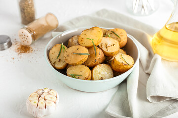 Bowl with baked potatoes and rosemary on light background
