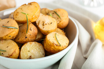 Bowl with baked potatoes and rosemary on light background, closeup