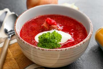 Bowl of tasty borscht with sour cream on dark background
