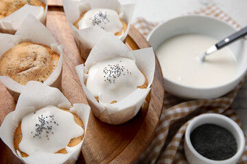 Wooden board with delicious glazed poppy seed muffins on table, closeup