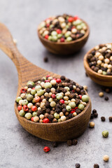 Peppercorn mix in a wooden bowl on grey table.