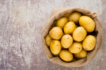 Sack of fresh raw potatoes on wooden background, top view.