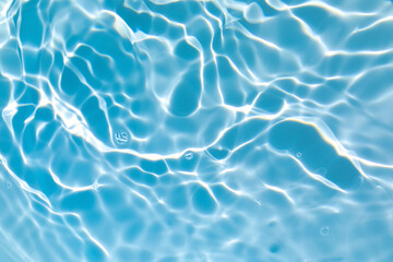 De-focused blurred transparent blue colored clear calm water surface texture with splashes and bubbles. Trendy abstract nature background. Water waves in sunlight with copy space.