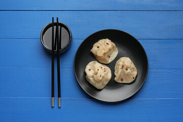 Plate with tasty dumplings, chopsticks and bowl of sauce on color wooden background