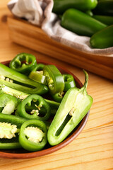 Plate with cut green jalapeno peppers on wooden background, closeup