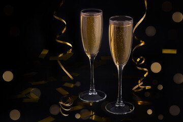 Two glasses of champagne on a black background with golden bokeh and serpentine.