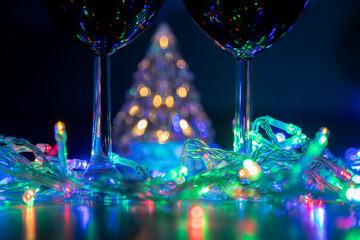 two glasses on the background of a shining Christmas tree and a multi-colored garland on a dark night background. New Year celebration...