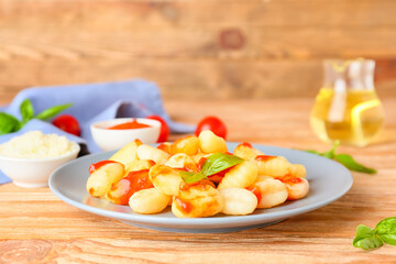 Delicious gnocchi with tomato sauce in plate on wooden table