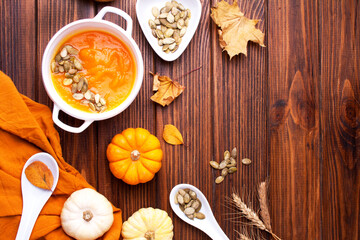 White plate with pumpkin soup and autumn leaves on a wooden table. Top of view