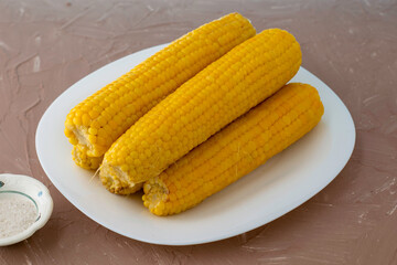 corn cooked on the cob on a white plate, next to a salt shaker with salt