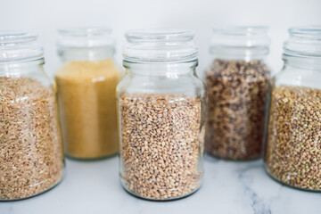 clear pantry jars with different types of grains in them including quinoa rice buckwheat couscous and barley, simple ingredients concept