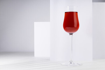 Red port wine in rich high glass in sunlight with shadow in modern minimal abstract white interior with geometric spaces.