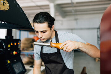 Close up of young man with spatula checking quality of freshly roasted arabica coffee beans