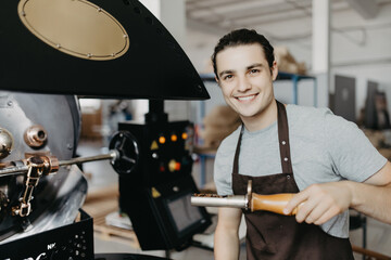 Close up of young man with spatula checking quality of freshly roasted arabica coffee beans