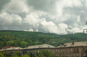 Three houses standing near high green hills. The sky is covered with dark clouds
